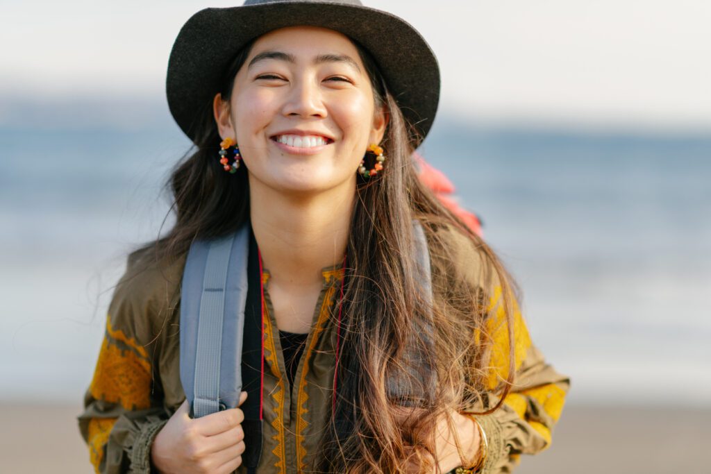 A close-up portrait of a happy female solo traveler at the beach.